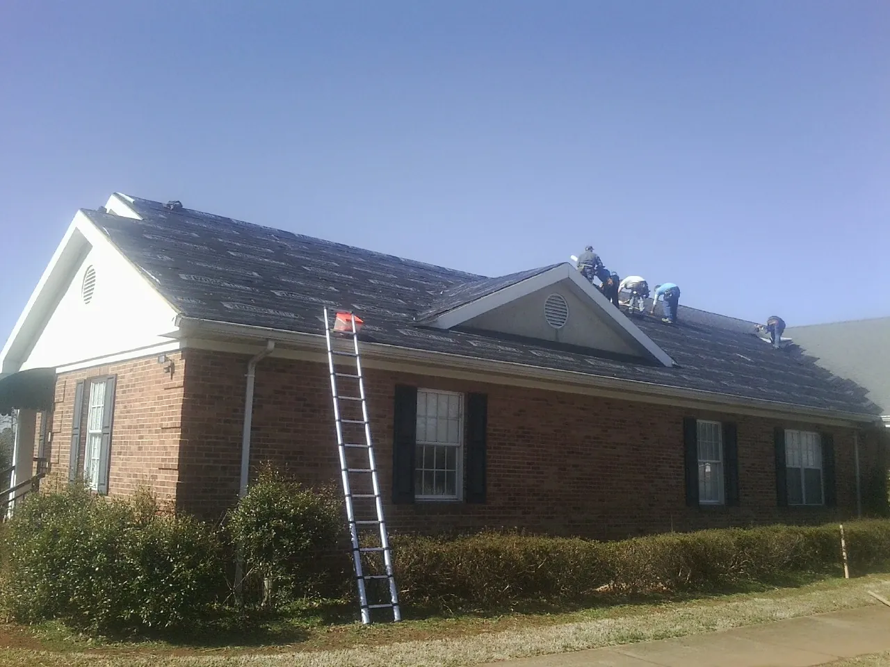 Crew tearing shingles off a brick ranch roof with a ladder set — Emergency Roof Repair work by our crew in Netcong