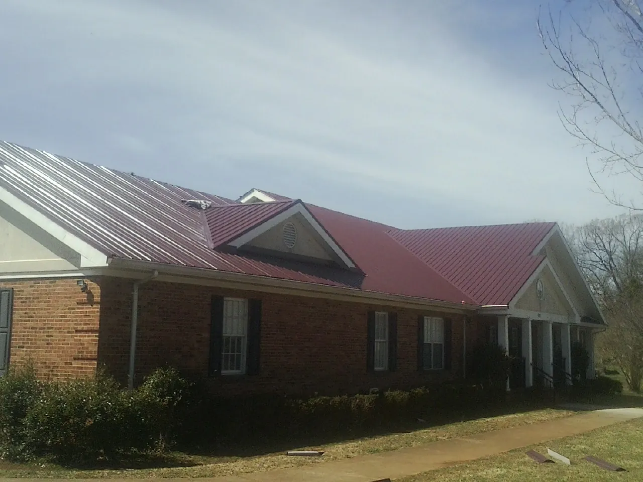 Red metal roof with gabled entries on a long brick building, from a Hail Damage Roof Repair job in Netcong