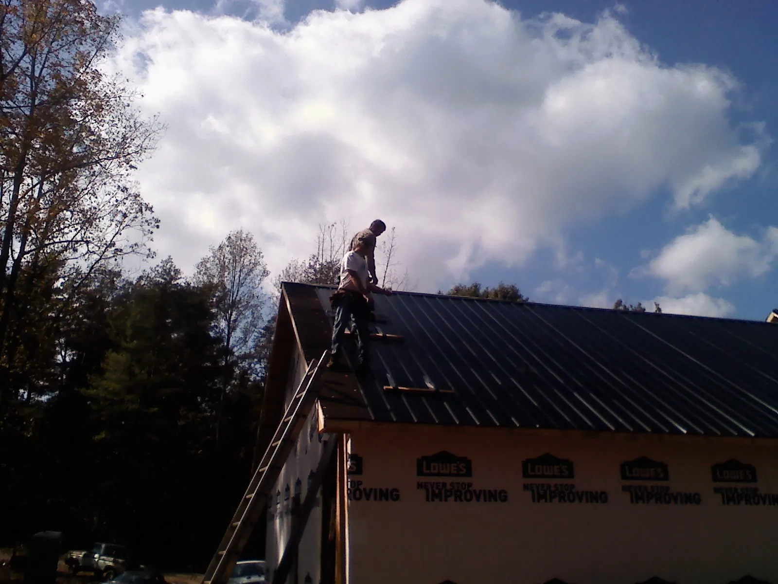 Roofer fastening dark metal panels high against a cloudy sky, from a Roof Inspection job in Netcong