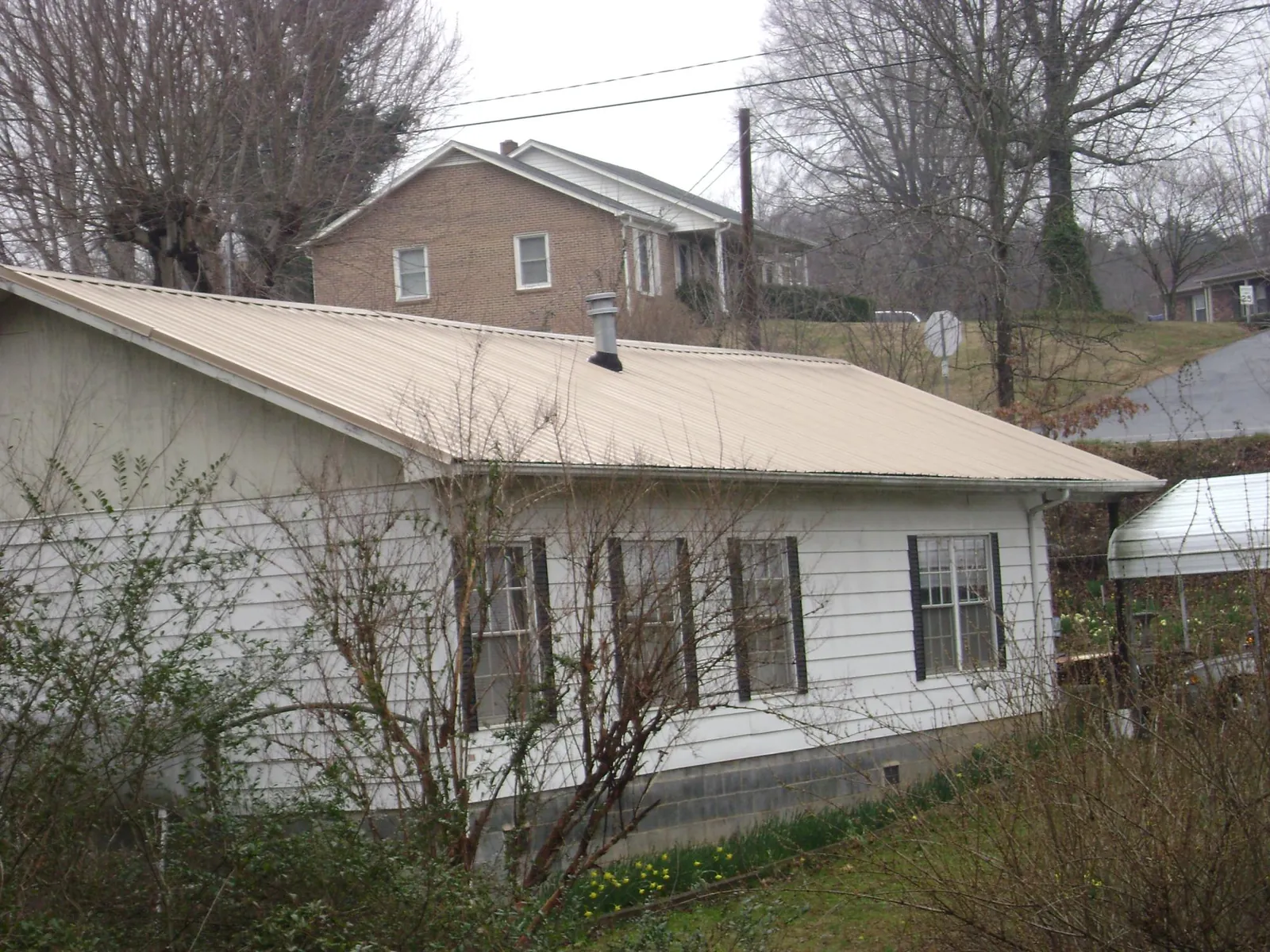 Tan metal roof on a white sided house set into a hillside — Commercial Roofing by Roofing Brothers in Netcong